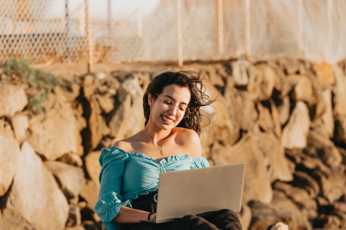Smiling woman works on her laptop outdoors.